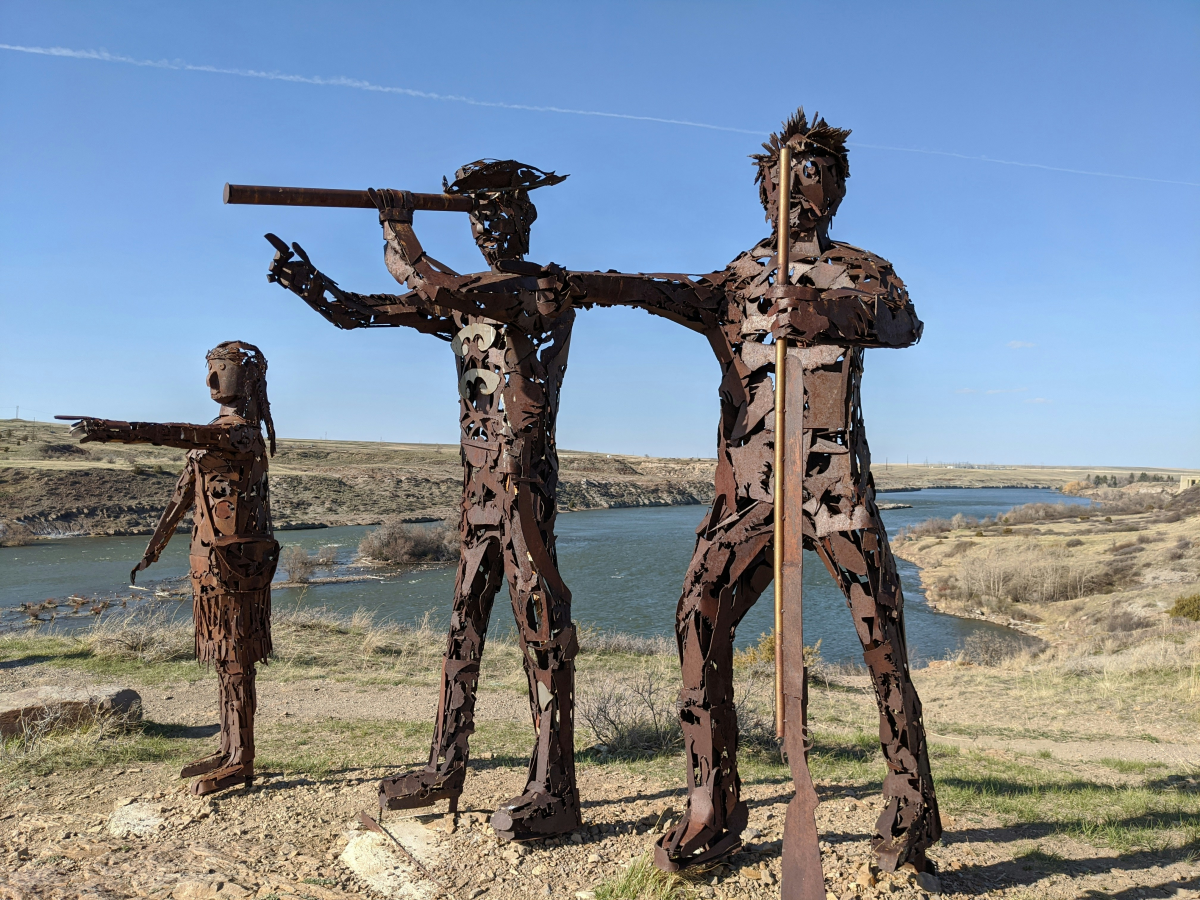 Sacagawea, Lewis és Clark fémből készült szoboralakjai egy dombtetőn, a távolba tekintve.